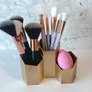 Può includere: Portapennelli per trucco dorato con sei pennelli e una spugna per trucco rosa. Il portapennelli ha una forma esagonale ed è diviso in quattro scomparti.