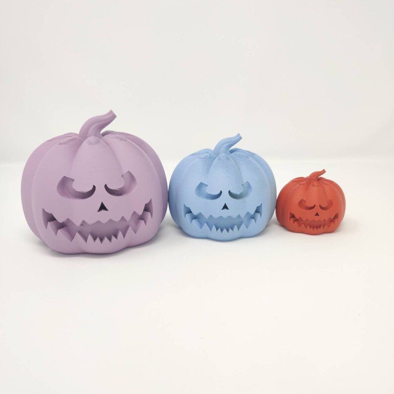 May include: Three Halloween jack-o'-lantern pumpkins, one purple, one light blue, and one orange, with carved faces.