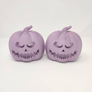 May include: Two purple ceramic pumpkin-shaped candle holders with carved faces.