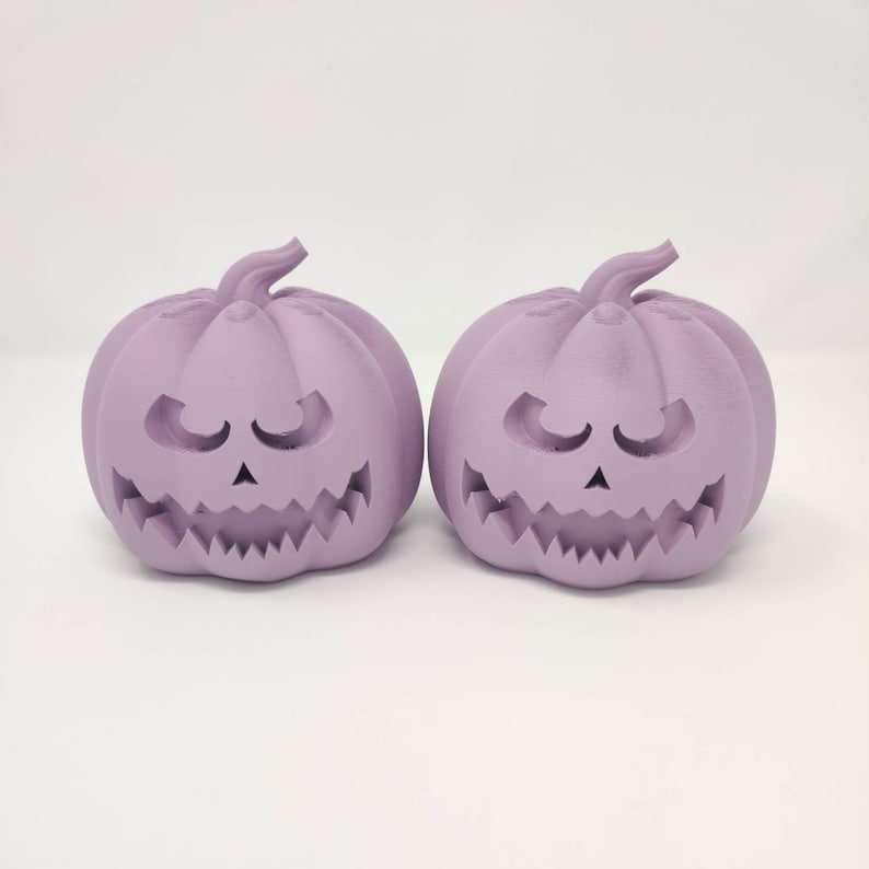 May include: Two purple ceramic pumpkin-shaped candle holders with carved faces.