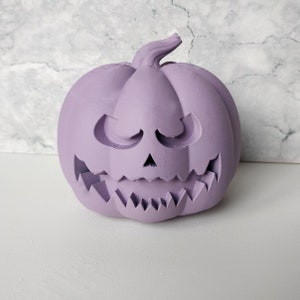 May include: A purple ceramic pumpkin with a carved jack-o'-lantern face. The pumpkin has a wide, toothy grin and a mischievous expression.