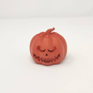 May include: A small, orange, 3D printed pumpkin with a carved jack-o'-lantern face.