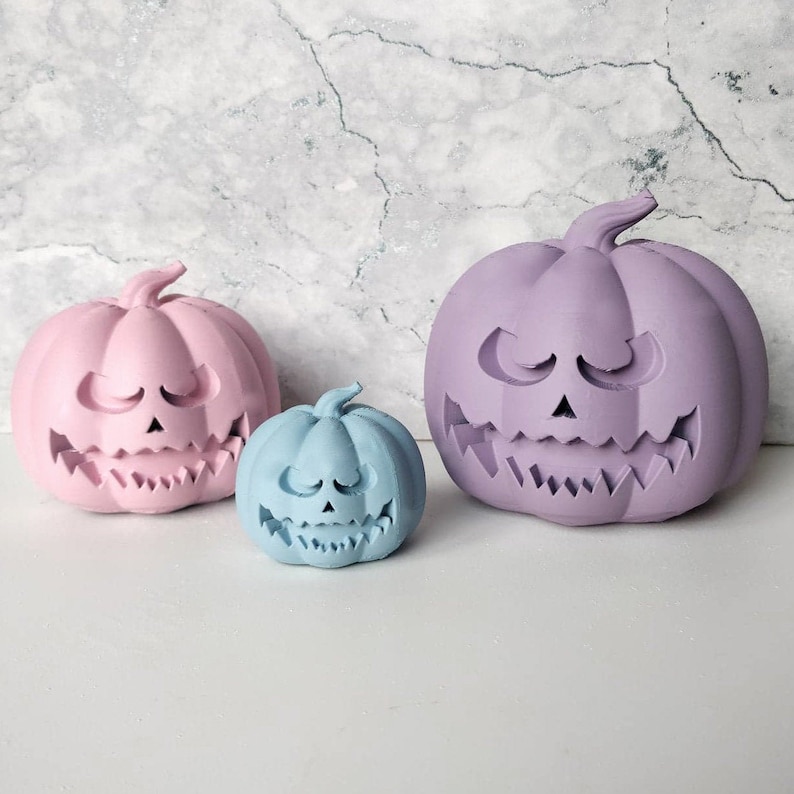 May include: Three Halloween jack-o'-lantern pumpkins in different sizes. The largest pumpkin is purple, the medium pumpkin is pink, and the smallest pumpkin is light blue.