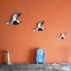 May include: A rustic fireplace mantel with a mosaic tile design featuring a bird. The mantel is made of weathered wood and has a wood-burning stove below. There are three decorative bird sculptures on the wall above the mantel.