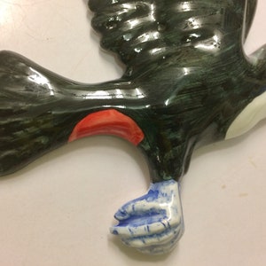 May include: A ceramic toucan figurine painted in black, green, white, red, and blue. The toucan is in flight with its wings outstretched. The toucan's beak is open and its eyes are closed.