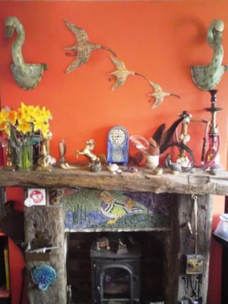May include: A rustic fireplace mantel with a mosaic tile design and a wood-burning stove. The mantel is decorated with various ceramic birds, a ceramic deer, and other decorative items.