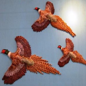 May include: Three decorative pheasant wall hangings in flight, featuring detailed feather patterns in shades of brown, orange, and cream. Each bird has a red head and is set against a light blue background, creating a rustic, nature-inspired aesthetic.