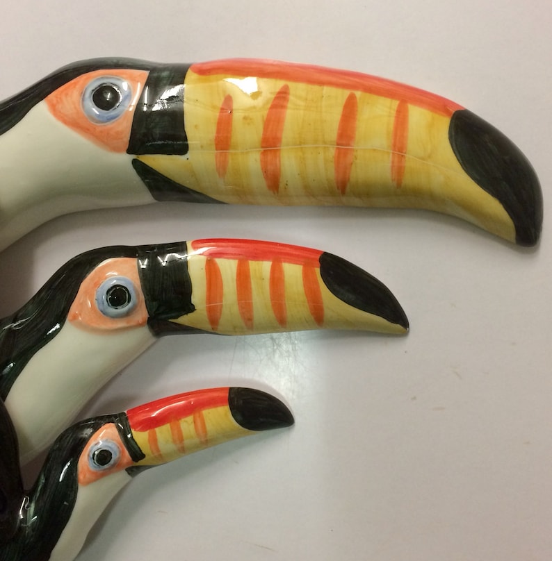 May include: Three ceramic toucans of varying sizes, painted in bright colours with black, yellow, orange, and white accents. The toucans are arranged in a cascading pattern, with the largest toucan at the top and the smallest toucan at the bottom.