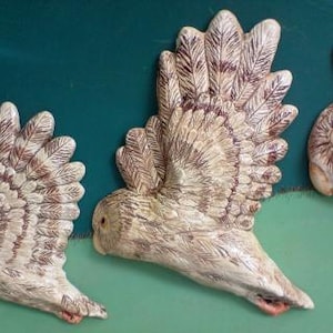 May include: Three ceramic owl sculptures with brown and white painted feathers. The owls are in flight with their wings spread out.