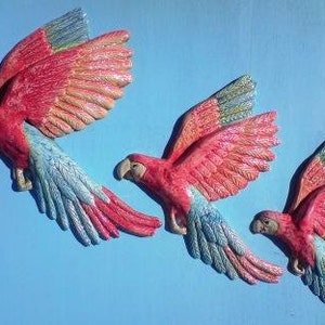 May include: Three ceramic macaw parrots in flight, painted in red and blue with a shimmery finish. The parrots have detailed feathers.