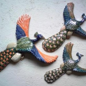 May include: Three ceramic peacocks with blue, green and orange paint. The peacocks are in flight with their tails spread out.