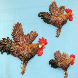 May include: Three rooster wall decor pieces in various sizes. The roosters are brown and black with red combs and wattles. They are in a flying pose with their wings spread.
