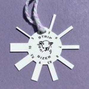 May include: White plastic knitting needle gauge with a sheep illustration and the text "A Stripe Sizer". The gauge has numbers from 4 to 10.
