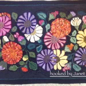 Peut inclure: Tapis rectangulaire fait à la main avec un fond bleu foncé. Le tapis présente un motif floral vibrant avec des fleurs roses, violettes, oranges, jaunes et blanches, entourées de feuilles vertes. Le texte "hooked by Janet Crook" est en bas.