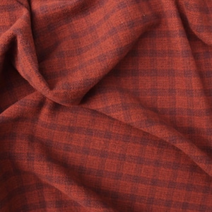 May include: A piece of fabric featuring a dark red and black plaid pattern. The material has a soft, slightly fuzzy texture and is draped in folds, creating deep shadows and highlights across the surface of the checkered textile design.
