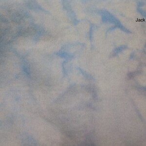 May include: A close-up of a light blue and white tie-dye fabric with a subtle purple hue. The fabric has a soft, textured feel.