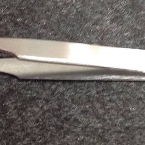 May include: A silver metal eyelash tweezer with a curved tip and a straight handle.