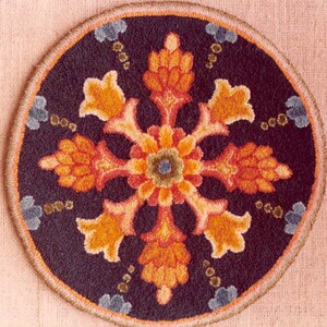 May include: Circular rug with a dark blue background and a central floral design in shades of orange, yellow, and red. The design is surrounded by a border and small blue floral accents. The rug is likely made of wool or a similar material.