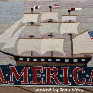 May include: A rectangular rug featuring a detailed depiction of a sailing ship with white sails and an American flag. The word "AMERICA" is prominently displayed in red letters at the bottom, set against a blue background.