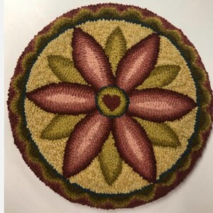May include: A round, handmade rug with a floral design. The rug features a central flower with burgundy petals and a heart-shaped center. Green leaves and a yellow background surround the flower. The border is a scalloped design in shades of green and burgundy.
