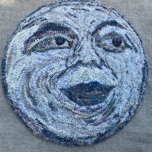 May include: A round, hand-hooked rug featuring a smiling face design. The rug uses shades of blue, gray, and purple to create the face, with a prominent mouth and eyes. The rug is made of looped yarn and has a textured appearance.