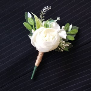 Könnte beinhalten: Ein weißes Blumen-Boutonniere mit grünen Blättern und einer braunen Bindfaden-Umwicklung.