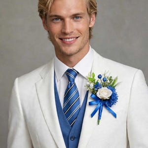 Op de afbeelding: Een wit colbert gedragen over een blauw vest en een wit overhemd met een blauwe gestreepte das. Een corsage met een witte roos, blauwe bloemen, groen blad en blauwe bessen is met een blauw lint op de revers van het jasje gespeld.