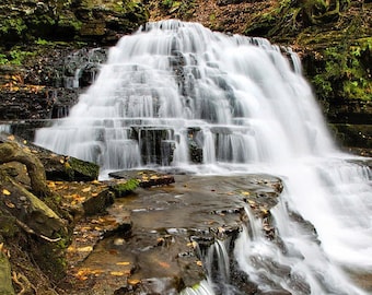 Peut inclure: Une cascade d'eau se déverse sur des rochers recouverts de mousse dans un cadre forestier luxuriant. L'eau est blanche et mousseuse, créant une sensation de mouvement et d'énergie. Les rochers sont bruns et gris, et les feuilles sont un mélange de vert et de jaune.