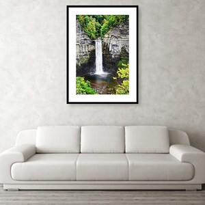 Peut inclure: Une photographie d'une cascade qui d&eacute;vale une falaise rocheuse, entour&eacute;e d'arbres verdoyants. L'eau est claire et blanche, et les rochers sont gris et bruns. La cascade est encadr&eacute;e par un cadre noir.