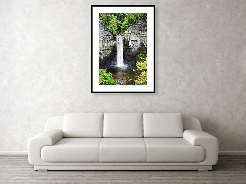 Peut inclure: Une photographie d'une cascade qui d&eacute;vale une falaise rocheuse, entour&eacute;e d'arbres verdoyants. L'eau est claire et blanche, et les rochers sont gris et bruns. La cascade est encadr&eacute;e par un cadre noir.