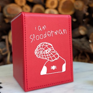 May include: A red rectangular deck box with a textured surface featuring a white line drawing of a masked character and the text "I am Spooderman" printed on the front. The box has visible stitching along the edges and a solid construction.