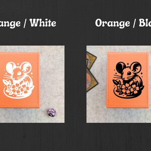 May include: Two orange card holders with a mouse and flower design. One has a white design, the other a black design. The text "Orange / White" and "Orange / Black" is above each card holder.