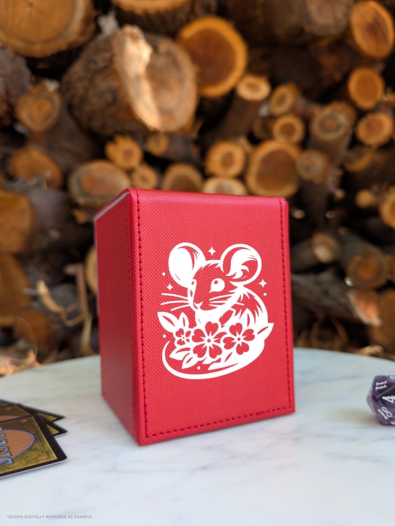 May include: A red card storage box with a white illustration of a mouse and flowers. The box is rectangular and appears to be made of a textured material. The background is blurred, featuring wood logs.