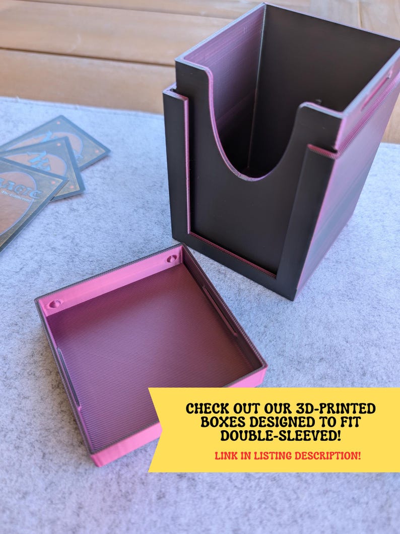 May include: A 3D-printed card storage box with a removable lid. The box is primarily black with pink accents and interior. The text "CHECK OUT OUR 3D-PRINTED BOXES DESIGNED TO FIT DOUBLE-SLEEVED! LINK IN LISTING DESCRIPTION!" is visible.