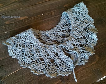May include: A delicate, light blue crocheted collar with a scalloped edge. The collar is tied at the back with a long, thin string.