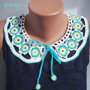 May include: A white crocheted collar with yellow and turquoise accents. The collar has a tie in the front and is worn on a blue sleeveless top.