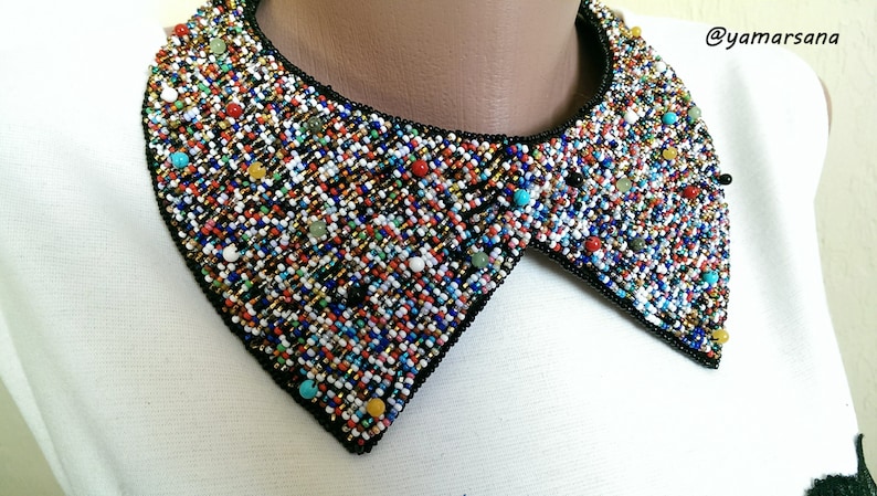 Peut inclure: Un collier de perles color&eacute; avec une bordure noire. Les perles sont dispos&eacute;es en un motif g&eacute;om&eacute;trique et sont de diff&eacute;rentes couleurs, notamment le rouge, le bleu, le vert, le jaune et le blanc.