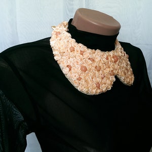May include: A black sheer blouse with a large, peach-colored fabric flower collar. The collar is made of many small fabric roses and beads.