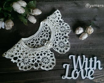 May include: White crocheted lace collar with a pearl button. The collar is on a wooden surface with the words "With Love" written on a white sign.