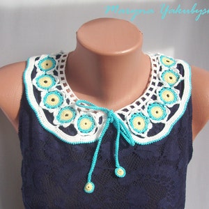 May include: White crocheted collar with yellow and turquoise flowers. The collar has a tie at the back.