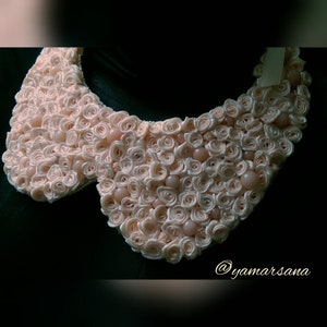 May include: A large, pink, fabric collar made of many small rosettes. The collar is decorated with small, round, light pink beads.