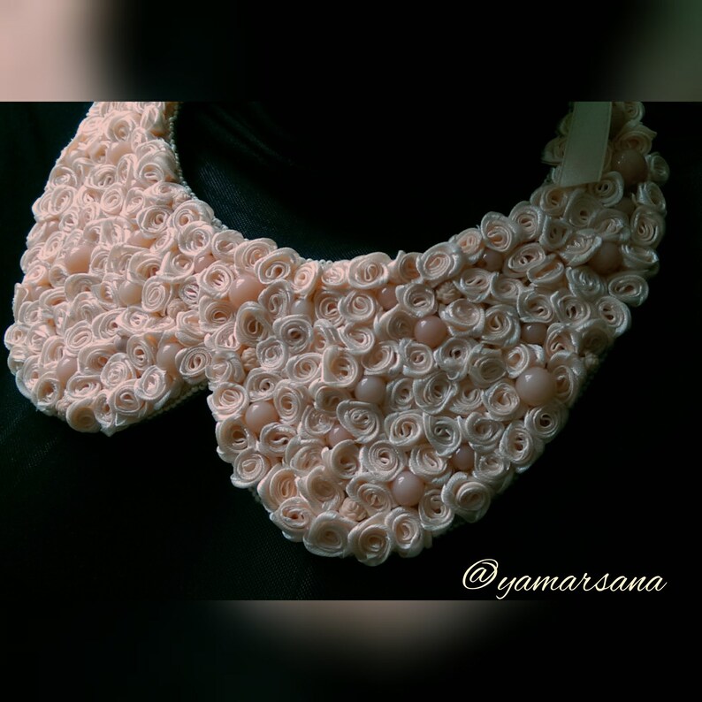 May include: A large, pink, fabric collar made of many small rosettes. The collar is decorated with small, round, light pink beads.