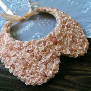 May include: A peach-colored fabric collar necklace made of fabric rosettes and peach-colored beads.