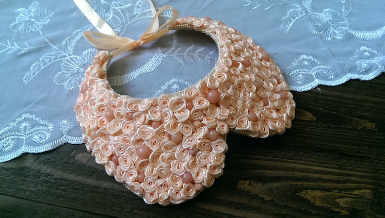 May include: A peach-colored fabric collar necklace made of fabric rosettes and peach-colored beads.