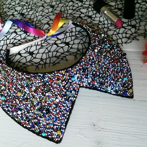 Peut inclure: Un collier ras de cou en perles color&eacute;es avec un dos noir. Le collier est compos&eacute; de petites perles multicolores et a une forme arrondie et ouverte.