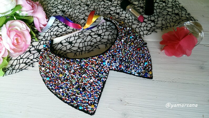 Peut inclure: Un collier ras de cou en perles color&eacute;es avec un dos noir. Le collier est compos&eacute; de petites perles multicolores et a une forme arrondie et ouverte.