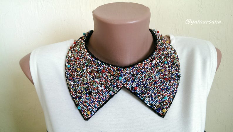 Peut inclure: Une chemise blanche avec un grand col perl&eacute; color&eacute;. Le col est fait de petites perles rondes de diff&eacute;rentes couleurs, notamment bleu, rouge, vert et jaune. Le col est fix&eacute; &agrave; la chemise avec une doublure en tissu noir.