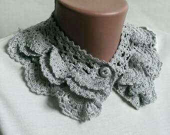 May include: A silver crocheted collar with a button closure. The collar is made of delicate, lacy fabric and has a ruffled design.