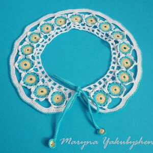 May include: White crocheted collar with blue and yellow accents. The collar has a tie closure and is decorated with a repeating pattern of small circles.