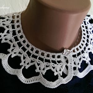 Puede incluir: Cuello blanco de ganchillo con borde festoneado y un intrincado dise&ntilde;o calado. El cuello se muestra sobre un maniqu&iacute; y se coloca sobre un vestido azul oscuro. Un delicado accesorio hecho a mano.